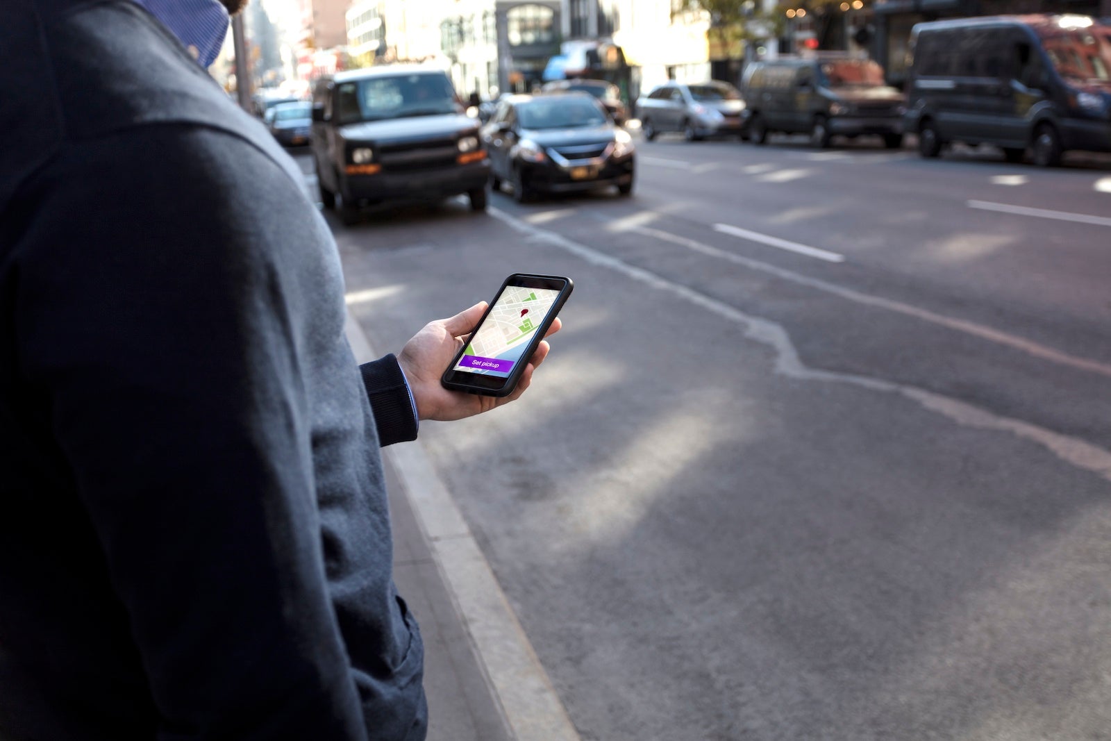 Young man holding cell phone waiting for car